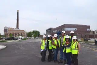 People in yellow vests and hardhats stand outside